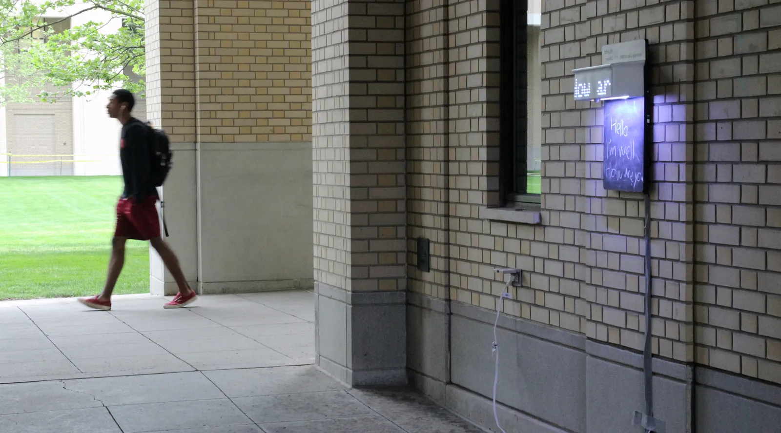 Photo showing the bPolite board mounted on a exterior wall of a building with a pedestrian walking by in the background.