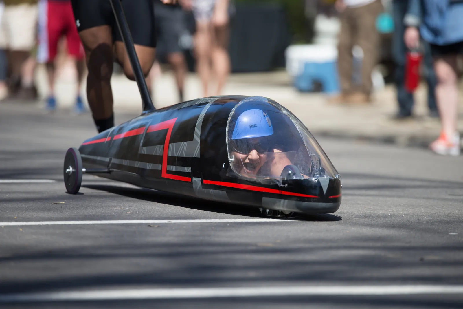 Photo showing a missile-shaped small vehicle with a windshield. A person wearing a helmet is inside laying prone controlling a steering mechanism.