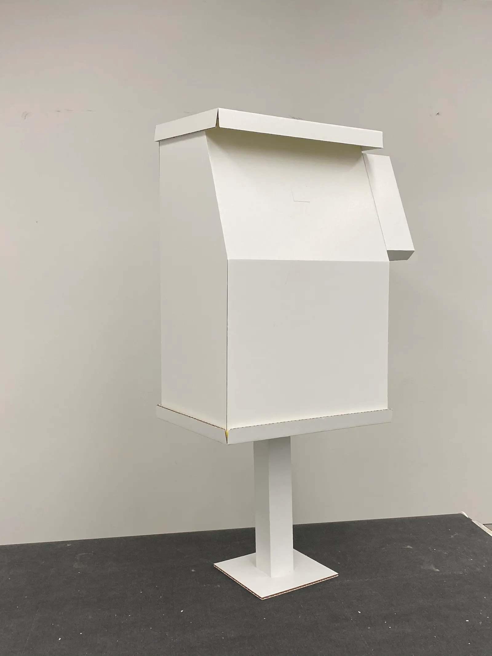 Photograph of a full-sized newspaper box mockup that is all-white and made of foamcore.