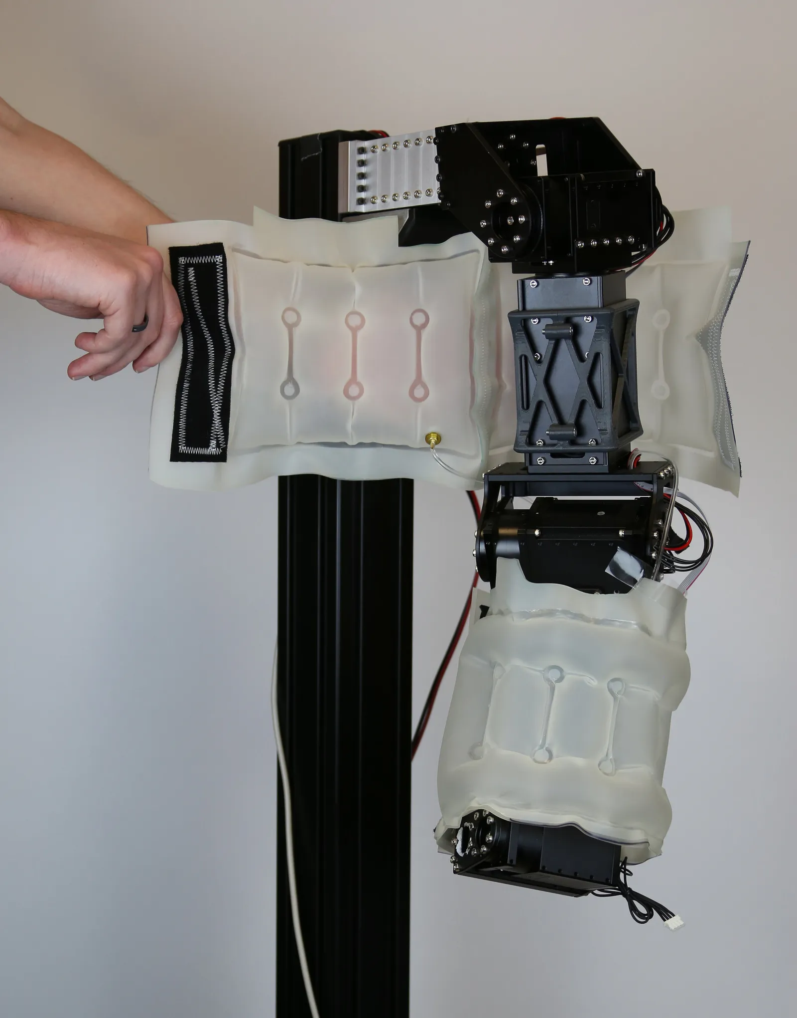 Photograph showing a black robot arm mounted on a stand. The "forearm" of the arm is covered with an air bubble. A person's hand holds an unfolded air bubble to expose the upper arm of the robot.