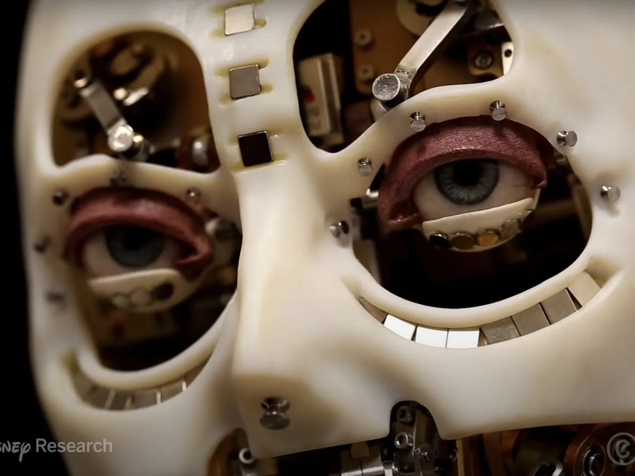 Close up photo showing the eyes of a mechanial robot. The eyes are realistic and have eye lids, blue pupils while the rest of the face is made of white plastic.