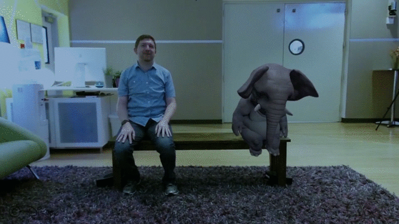 Animated GIF showing a person sitting on the magic bend and a virtual elephant sitting on the other end of the bench. The elephant is snoring as they sleep, and some wave lines show how the sound is coming from the bench as the elephant snores. The person reaches out to feel the bench and the vibrations.