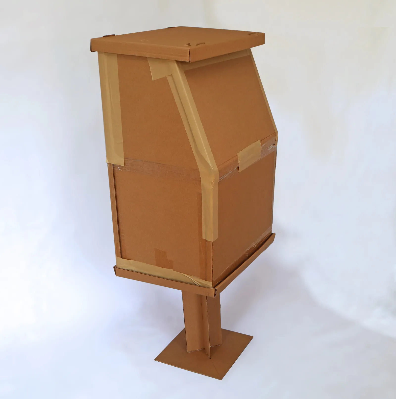 Photograph of a full-sized newspaper box mockup made of cardboard.