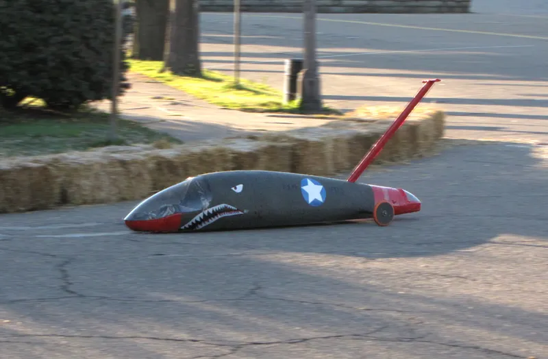 A missle-shaped vehicle painted to look like a world-war 2 fighter plane on a street.